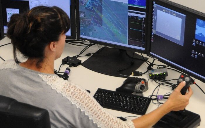A person sitting in front of monitors. She is testing flight control hardware with hardware-in-the-loop testing.